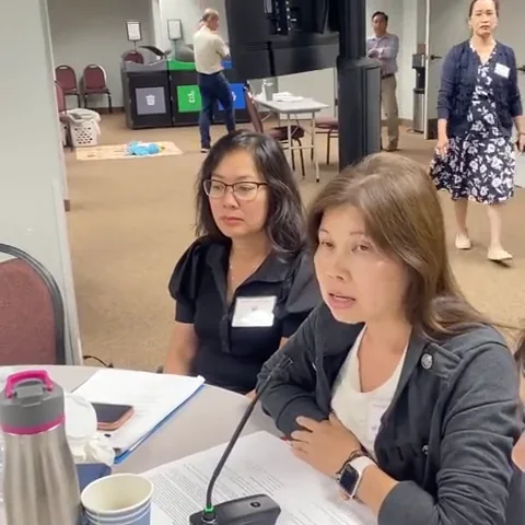 Two women with name tags in conversation at a table with a microphone