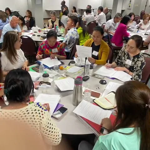 A round table of women with name tags writing notes on printed handouts